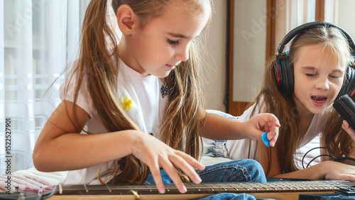 Little girl singing with microphone at home, concentrating, other child girl playing guitar.