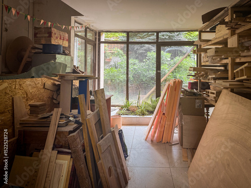 Fototapeta Naklejka Na Ścianę i Meble -  Sunlit carpentry studio with timber stacks, large windows, and raw planks arranged neatly for woodworking in a bright, natural-light-filled interior.