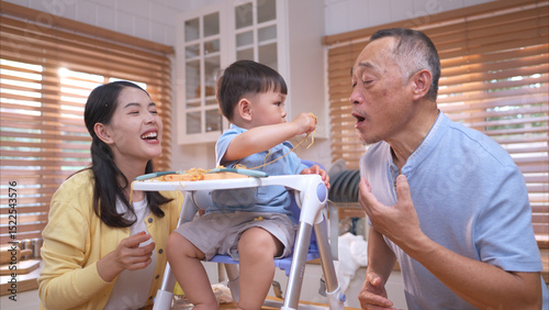 Happy Asian parents enjoying mealtime with their toddler in the kitchen