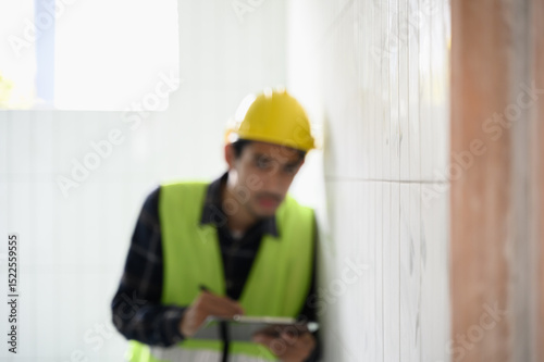 A professional Asian technician house building inspector inspects the aesthetic quality, finding defect and completeness of the architectural work of the house under construction using a checklist.