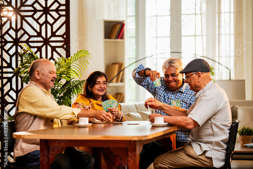 Indian senior citizens playing card game and bonding at cozy home dining table during reunion
