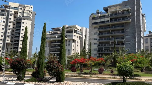 Modern urban area, lots of greenery, flowering trees. White multi-storey buildings, contemporary architecture. Rent and sale of real estate. 