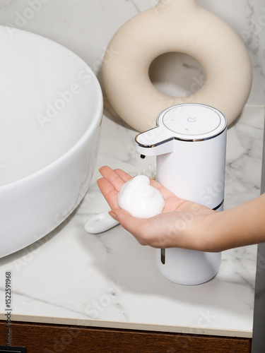 Woman using white automatic soap dispenser in bathroom