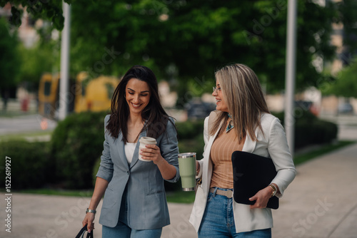 Wallpaper Mural Two businesswomen walking and talking outdoors, enjoying coffee break Torontodigital.ca