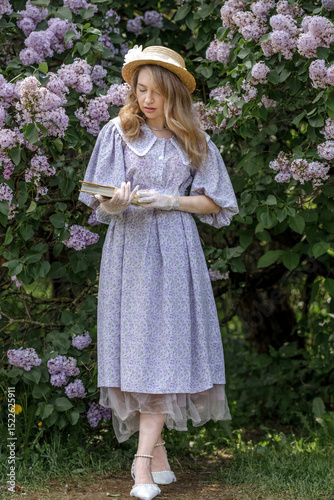 Vászonkép A beautiful young blonde woman, against a background of blooming lilacs, in a lilac vintage dress