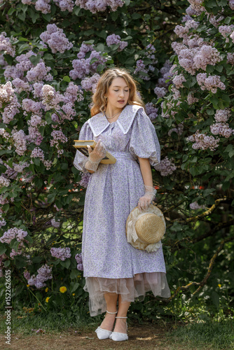 A beautiful young blonde woman, against a background of blooming lilacs, in a lilac vintage dress. A walk in the park.