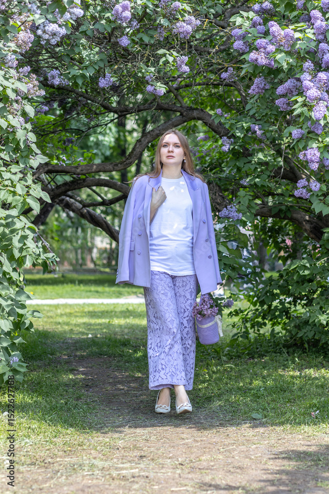 A beautiful young blonde woman, against a background of blooming lilacs, in a lilac trouser suit. Femininity and nature. A beautiful young blonde woman, against a background of blooming lilacs, in a lilac trouser suit. Femininity and nature.