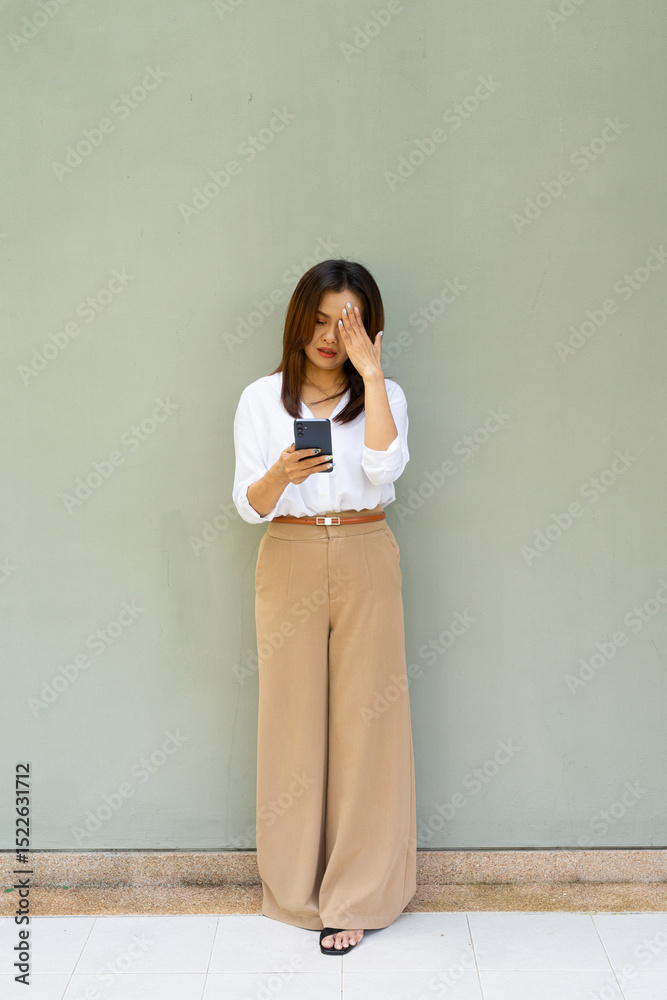 Fototapeta premium Full length portrait of woman standing in front of wall wearing business clothes using mobile phone