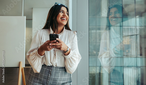 Fotografie Confident businesswoman standing by the window smiling and reflecting success an
