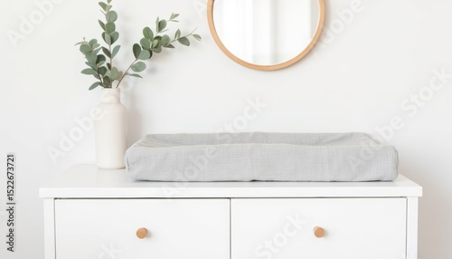Changing pad on white dresser with mirror and greenery in background   photo