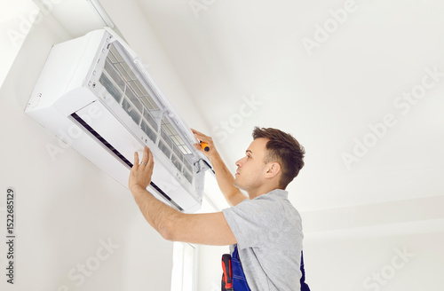 Air conditioning indoor unit installed by qualified installation technician. Professional young electrician maintaining, cleaning modern air conditioner on wall, room repairing, installing conditioner photo