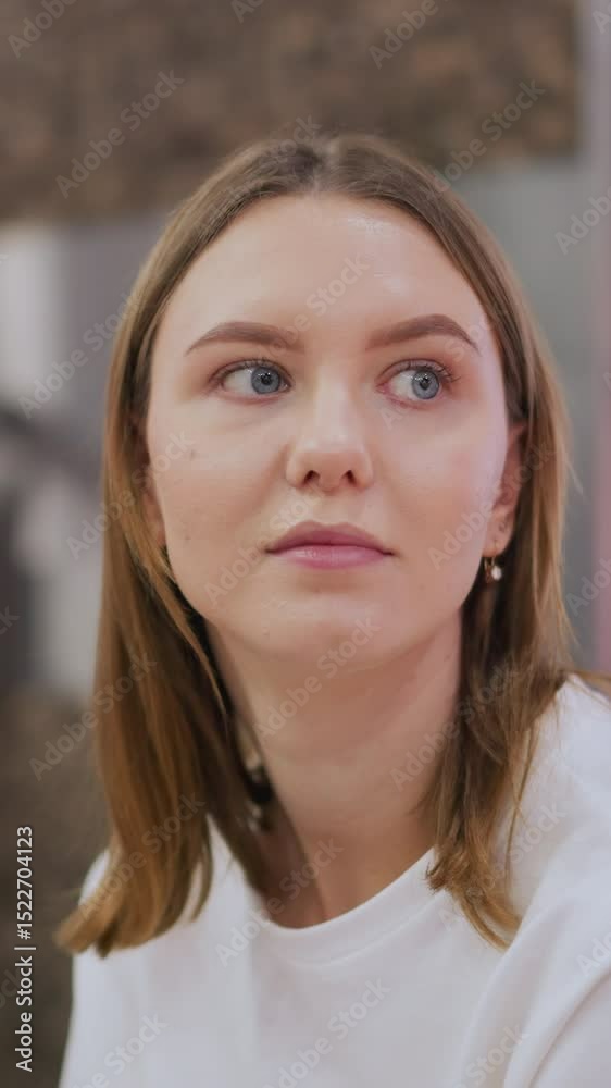 Young woman sitting indoors with a contemplative look, surrounded by subtle blue light reflections and warm tones in a modern space Young woman sitting indoors with a contemplative look, surrounded by subtle blue light reflections and warm tones in a modern space