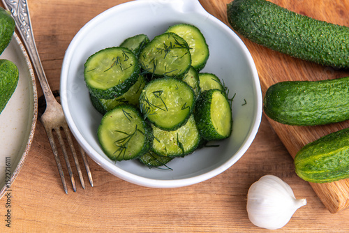 Organic cucumbers slices in a ceramic white bowl on a wooden table.
