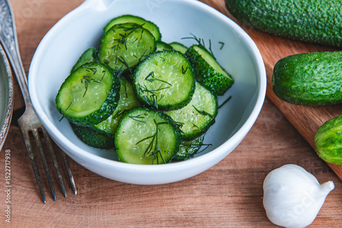 Organic cucumbers slices in a ceramic white bowl on a wooden table.