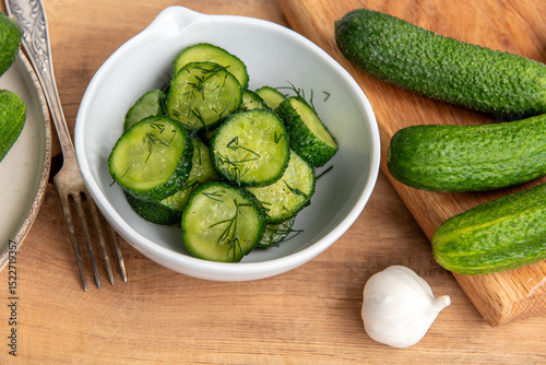 Organic cucumbers slices in a ceramic white bowl on a wooden table.