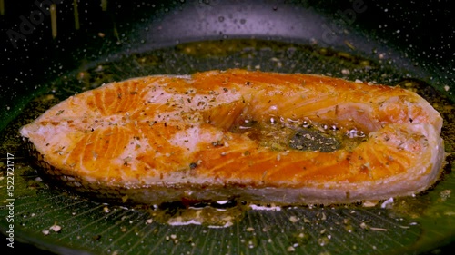 Salmon is being fried in a black iron pan with herbs, pepper and thyme.