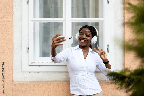 Positive black girl taking self-portrait photograph while listening to music.