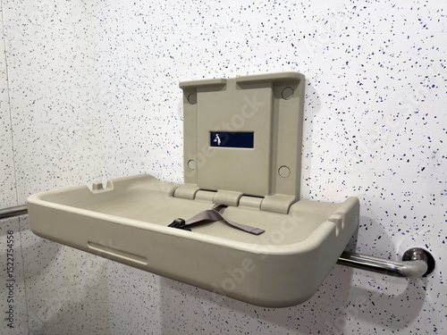 Open baby changing station with safety strap mounted on a public restroom wall. Practical hygienic facility designed for parents with infants in modern urban infrastructure