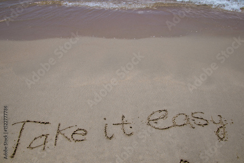 Fototapeta Naklejka Na Ścianę i Meble -  Words written in sand. The words TAKE IT EASY written in the sand on the beach.