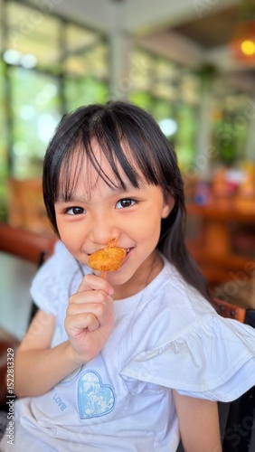 Happy cute Asian little girl holding fried chicken nugget to eat in restaurant, kid enjoying fast food concept.