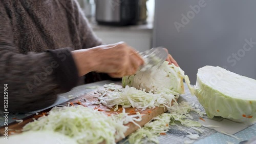Elderly woman skillfully chops fresh cabbage on a wooden cutting board, preparing ingredients for a healthy meal