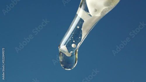 Macro shot of a white serum drop falling from a transparent dropper against a clear sky background