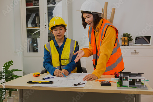 An Asian female engineer reviews and discusses detailed house construction plans  structural integrity, design accuracy, and successful project execution.