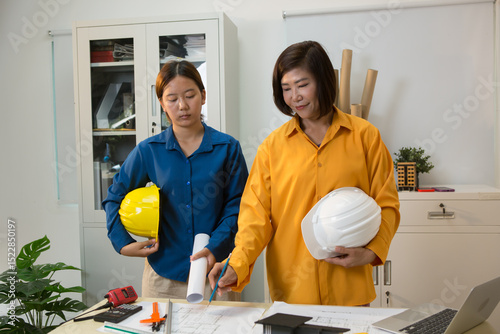 An Asian female engineer reviews and discusses detailed house construction plans  structural integrity, design accuracy, and successful project execution.