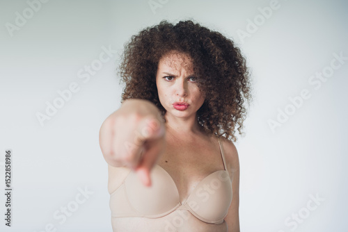 Confident young woman with curly brown hair pointing emphatically against a white background, expressing empowerment and self awareness photo