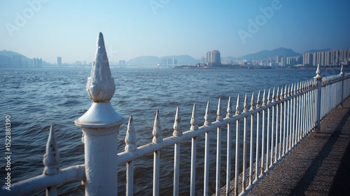 High-resolution photograph of a white metal fence with decorative slender bars along the quay, showcasing a serene cityscape in the background and tranquil sea water in the foreground