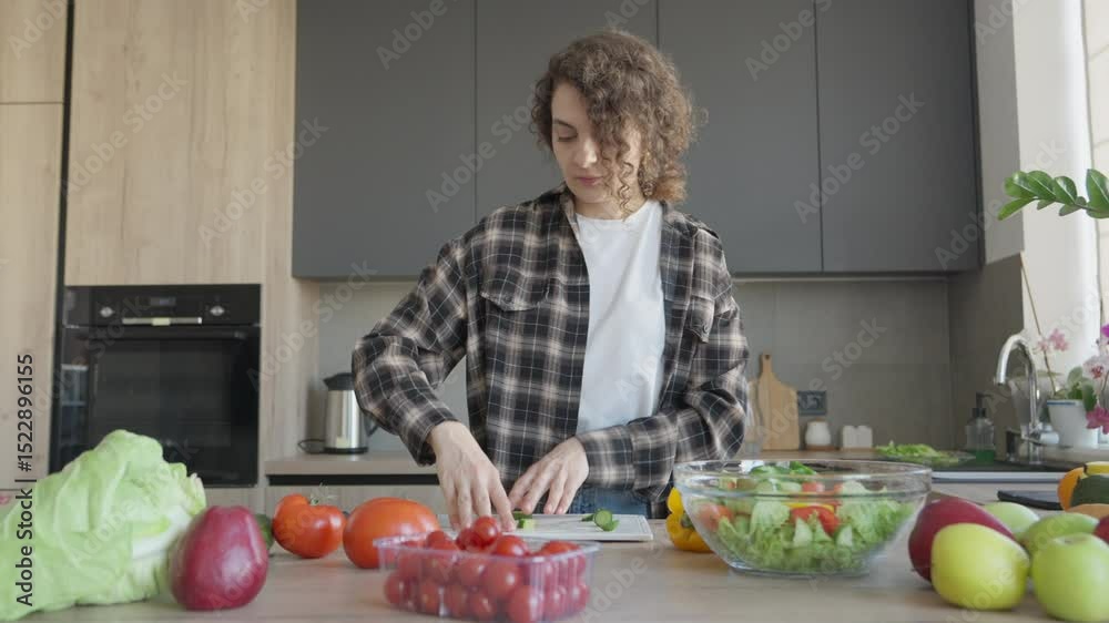 Adding Sliced Cucumber Into Bowl With Fresh Vegetable Salad In Bright Kitchen Adding Sliced Cucumber Into Bowl With Fresh Vegetable Salad In Bright Kitchen