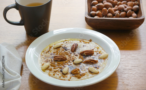 Healthy gluten free porridge cooked from buckwheat and corn semolina and served on white plate with cinnamon, maple syrup, butter and nuts. Morning porridge with mug of tee and nuts on wooden table.