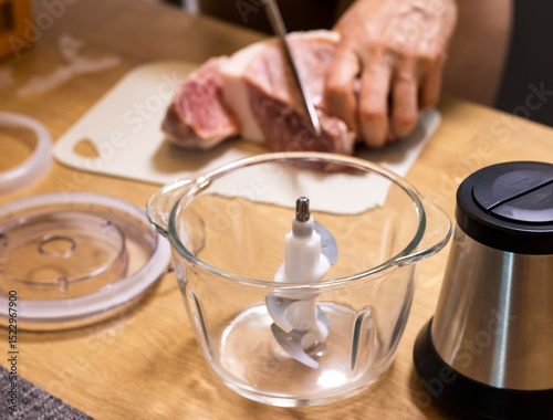 Woman cuts the meat, prepares it to grind it in electrical chopper. Food