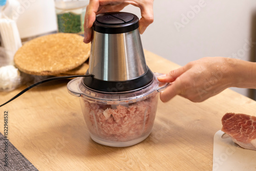 Woman mince the meat in the electrical chopper on the kitchen counter top. Cooking