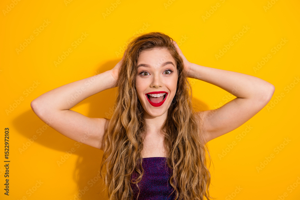 Fototapeta premium Cheerful young woman expressing excitement and joy with a vibrant smile and stylish wavy hair against a bold yellow background