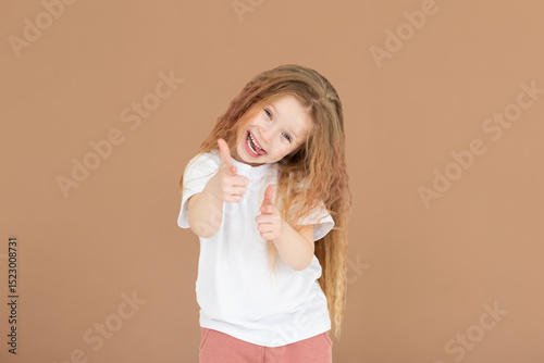 Young happy woman she wears white t-shirt casual clothes point index finger camera on you motivating encourage isolated on brown background studio. Lifestyle concept