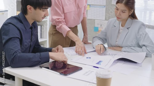 A focused team of Asian business professionals gathers around a conference table in a modern corporate office, deeply engaged in a financial consultation meeting. Surrounded by laptops, printed report