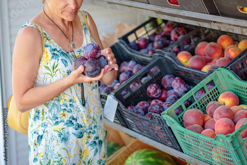Unrecognisable mature woman choosing fruits in street shop in resort town. Summer healthy shopping in farm store