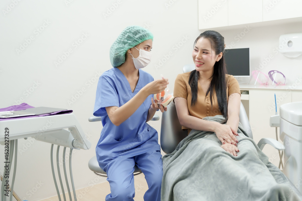 Obraz premium asian female dental assistant in blue uniform demonstrates toothbrushing technique using orthodontic model with braces to asian adult female patient in clean clinic after scaling session