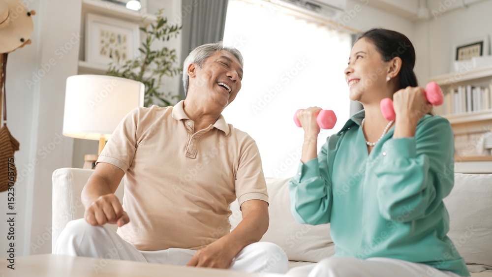Fototapeta premium Happy elderly couple exercising together with dumbbells at home, focusing on muscle strength, joint health, and physical wellness for improved mobility and healthy aging. Retirement concept. Myrmidon.