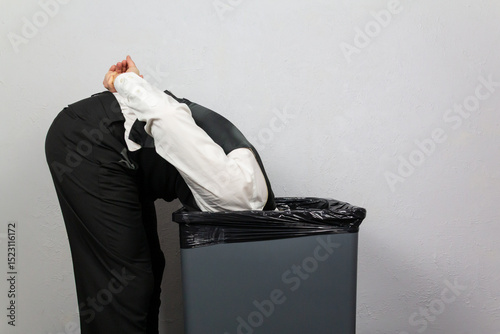 Businessman With His Head in Trash Can as if Inspecting It. Over a Barrel. Concept of Being Sacked or Fired.