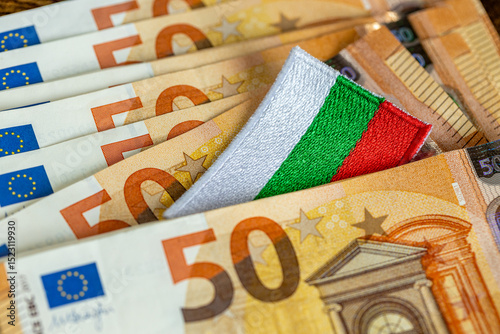 Fototapeta Naklejka Na Ścianę i Meble -  Admission of Bulgaria to the euro zone in 2026. The flag of Bulgaria sticking out from between the Euro banknotes. Financial concept. Close Up