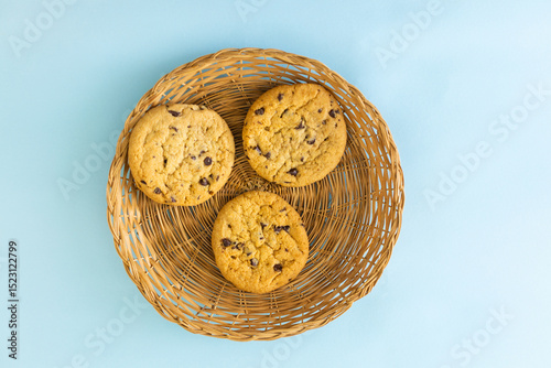 Three chocolate chip cookies in a basket on a blue background