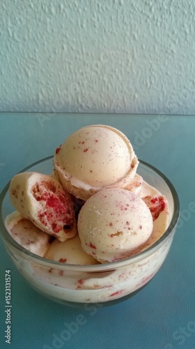 Bowl full of strawberry flavored vanilla ice cream scoops, with a textured wall in the background