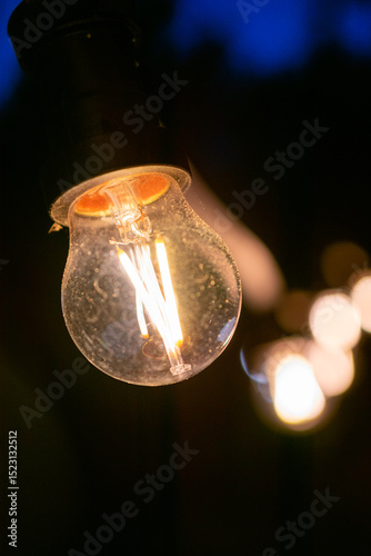 Light bulb is lit up in the dark. The light is warm and inviting. The bulb is glowing with a soft, yellow light.