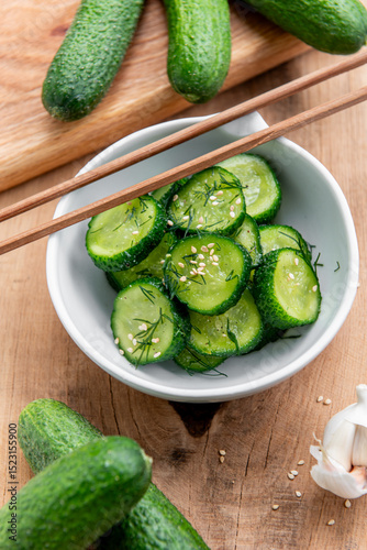  Sunomono, japanese cucumber salad. Sliced cucumbers with asian dressing of soy sauce, rice vinegar, sesame oil, sugar nd dill in white bowl on wood table. 