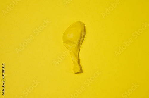 One yellow deflated balloon lies on a yellow background