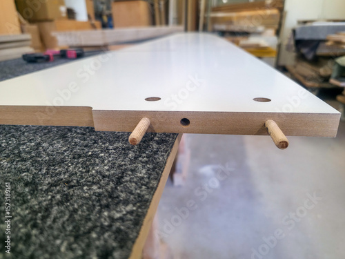 Detailed view of woodworking process showing dowel joint on a laminate board in a workshop environment
