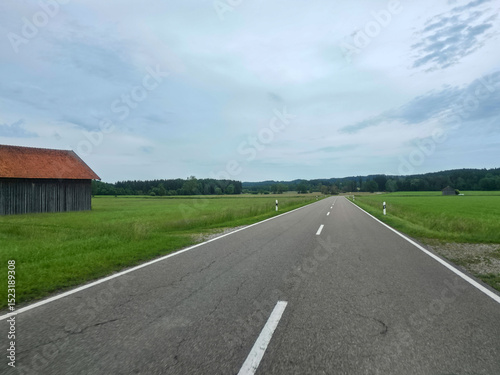 Scenic countryside road stretches through lush fields under a cloudy sky in rural landscape
