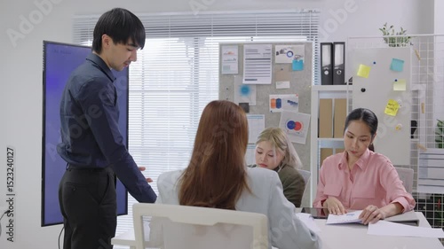 A focused team of Asian business professionals gathers around a conference table in a modern corporate office, deeply engaged in a financial consultation meeting. Surrounded by laptops, printed report